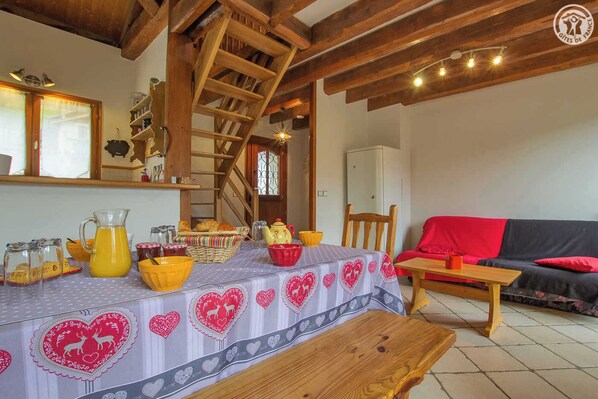 Ein gemütlicher Essbereich mit einem Holztisch, gedeckt für eine Mahlzeit, einer Treppe und einem Wohnzimmer mit einer Couch und einer roten Decke.