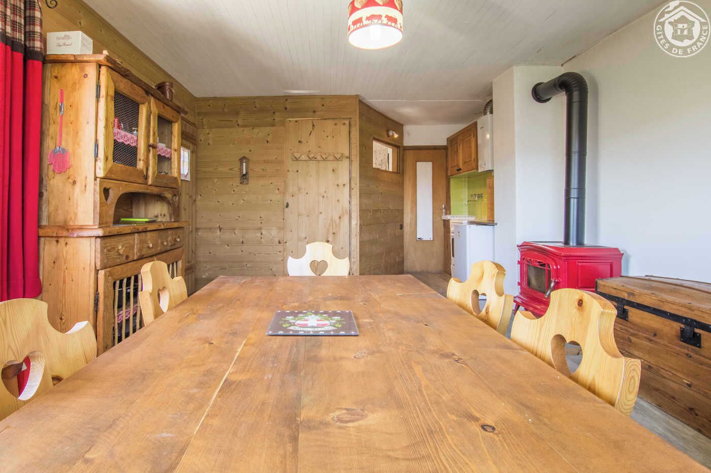 Una mesa de comedor de madera con sillas, una estufa roja y una cocina con armarios y un lavamanos.