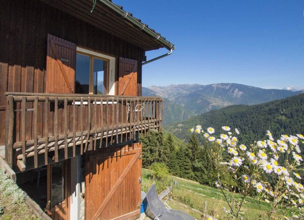 A wooden chalet with a balcony overlooking a mountainous landscape.