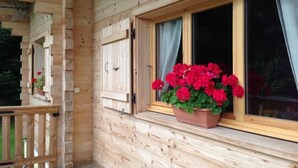 A wooden cabin with a window featuring a potted red flower arrangement. - CHALET LES AROLLES - HAUTELUCE LES SAISIES (HAUTELUCE LES SAISIES)
