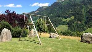 A wooden swing set in a grassy field with large rocks and a mountainous landscape in the background. - CHALET LES AROLLES - HAUTELUCE LES SAISIES (HAUTELUCE LES SAISIES)