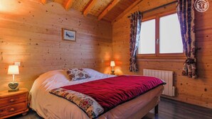 A cozy wooden cabin bedroom with a bed, two bedside lamps, and a window with curtains. - CHALET LES AROLLES - HAUTELUCE LES SAISIES (HAUTELUCE LES SAISIES)