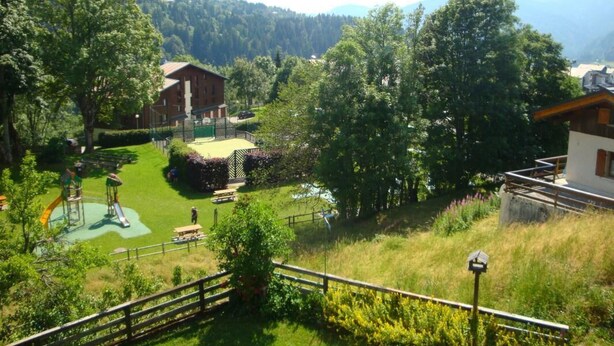 A rural landscape with a playground, a wooden house, and a fenced area.