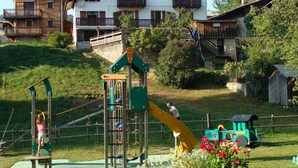 A playground with climbing structures and a slide, surrounded by houses and greenery.