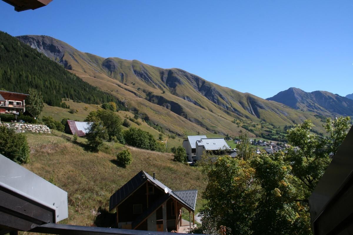 Eine gebirgige Landschaft mit einem kleinen Dorf, darunter Häuser mit geneigten Dächern und eine markante Holzhütte.