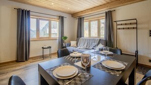 Un coin repas avec un plafond en bois, de grandes fenêtres, un canapé et une table dressée pour quatre personnes.