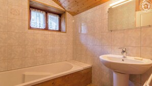 A bathroom with a bathtub, a sink, and a window with lace curtains. - CHEZ MARIE - LA TRINITE (LA TRINITE)