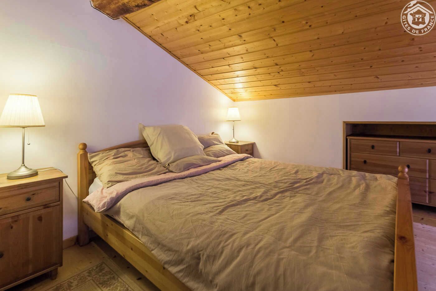 Une chambre à coucher avec un lit en bois, deux tables de chevet avec des lampes, une commode en bois et un plafond en pente.