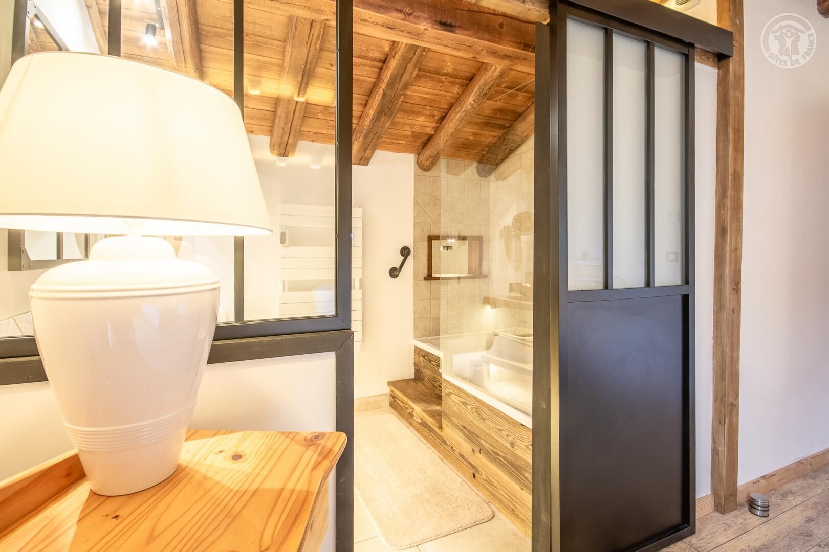 A bathroom with a wooden ceiling, a white bathtub, and a door with frosted glass panels.