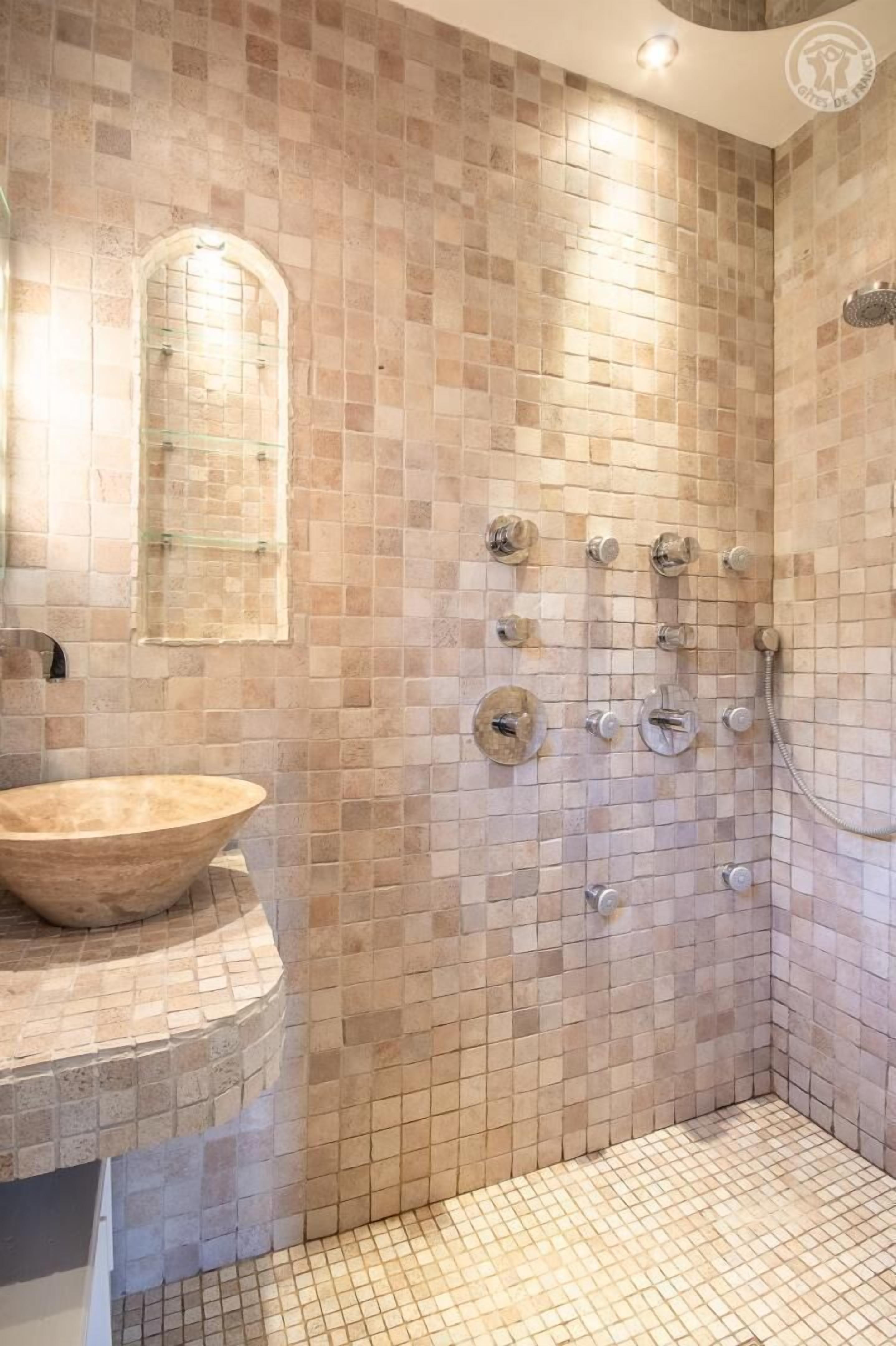 Ein Badezimmer mit freistehender Badewanne, einer Dusche mit mehreren Bedienelementen und einem gefliesten Boden.