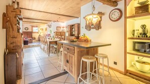 A rustic kitchen with wooden beams, a wooden bar counter, stools, and a clock on the wall. - CHALET LE COURTI - SAINTE FOY TARENTAISE (SAINTE FOY TARENTAISE)