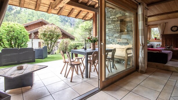 A modern chalet with a glass door leading to a patio area, wooden furniture, and a stone wall. - CHALET LE COURTI - SAINTE FOY TARENTAISE (SAINTE FOY TARENTAISE)