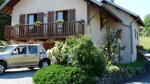 A two-story chalet with a balcony, a car parked in front, and lush greenery around. - LA FONTANETTE - PORTE DE SAVOIE (PORTE DE SAVOIE)