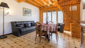 A cozy room with a wooden ceiling, a black leather sofa, a dining table with chairs, and a staircase. - LA FONTANETTE - PORTE DE SAVOIE (PORTE DE SAVOIE)