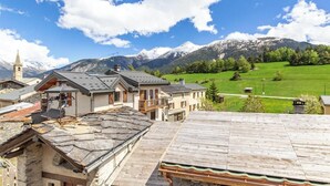 A mountainous landscape with a clear sky, a church with a bell tower, and a row of traditional buildings with sloped roofs. - Symphorose - Larch (VAL-CENIS)