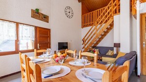 A dining area with a wooden table set for four, a staircase, and a sofa in the background. - Symphorose - Larch (VAL-CENIS)