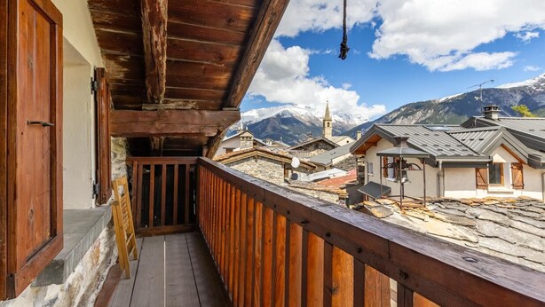 A wooden balcony with a view of a mountain village, stone buildings, and a church. - Symphorose - Larch (VAL-CENIS)