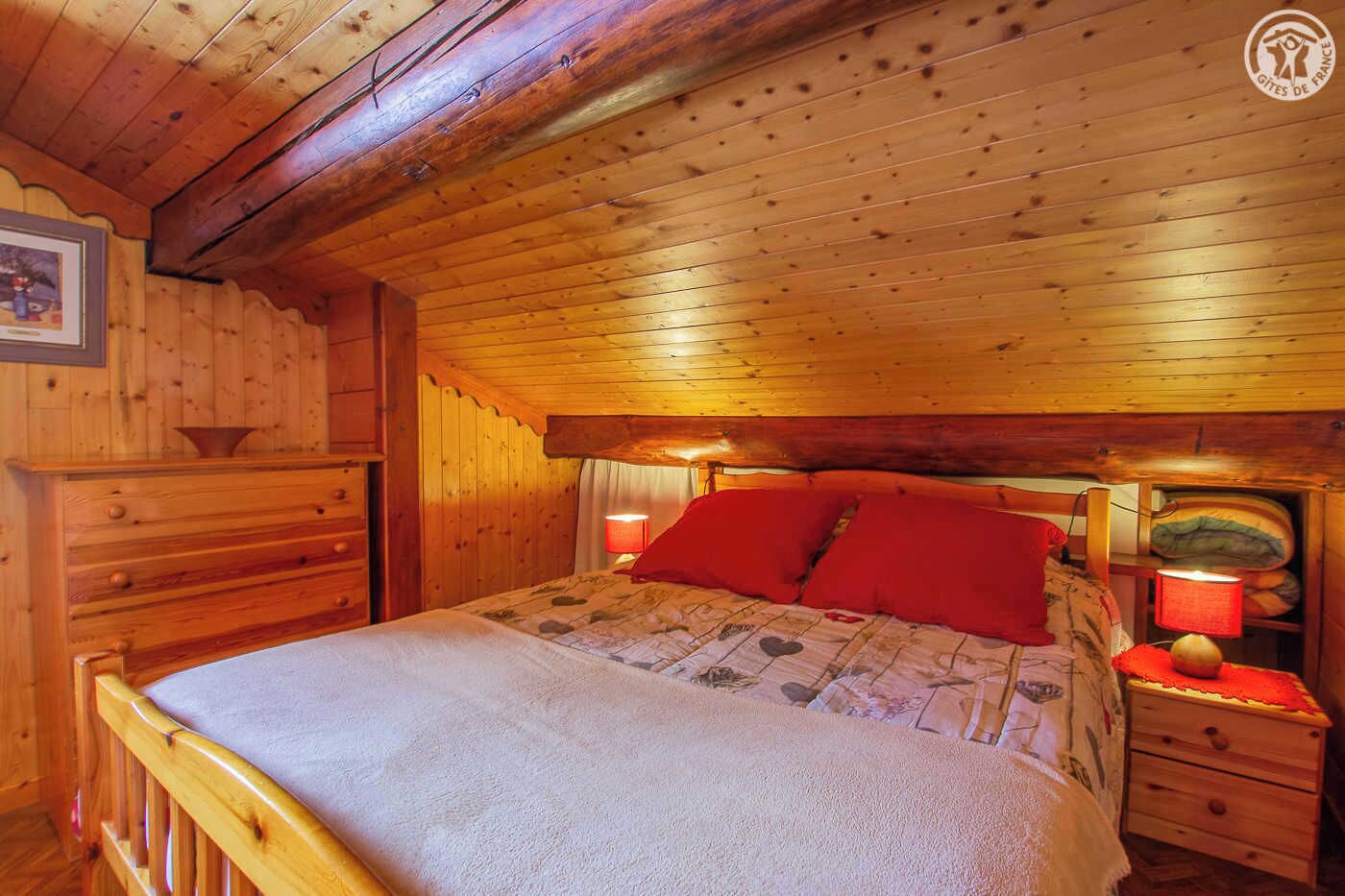 Une chambre confortable, aménagée dans un chalet en bois, avec un lit, des tables de chevet et une commode.