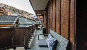Ein Holzbalkon mit einer Rattan-Couch und einem kleinen Tisch, mit Blick auf ein Dorf mit traditionellen Häusern.