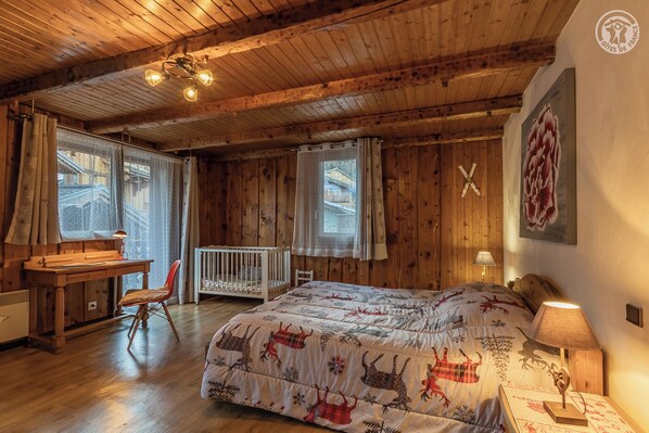 Een knus vertrek met houten wanden en plafond, een bed met een beddegoed met patroon, een bureau met stoel, en een wieg.