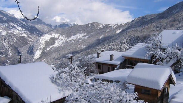 A snow-covered mountain village with rustic wooden houses and a clear view of the surrounding mountains.