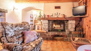 A cozy living room with a stone fireplace, wooden beams, and a television mounted above it.