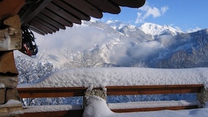 A wooden bench with snow accumulation in a mountainous area.