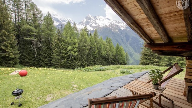 A wooden deck with a view of snow-capped mountains, a red exercise ball, and a grill.