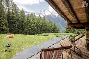 A wooden deck with a view of snow-capped mountains, a red exercise ball, and a grill.
