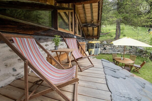 A wooden deck with striped lounge chairs, a small table, and a stone wall.