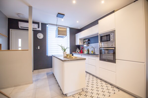 Une cuisine moderne avec des meubles blancs, un four à micro-ondes encastré et un petit îlot central agrémenté d’une plante.