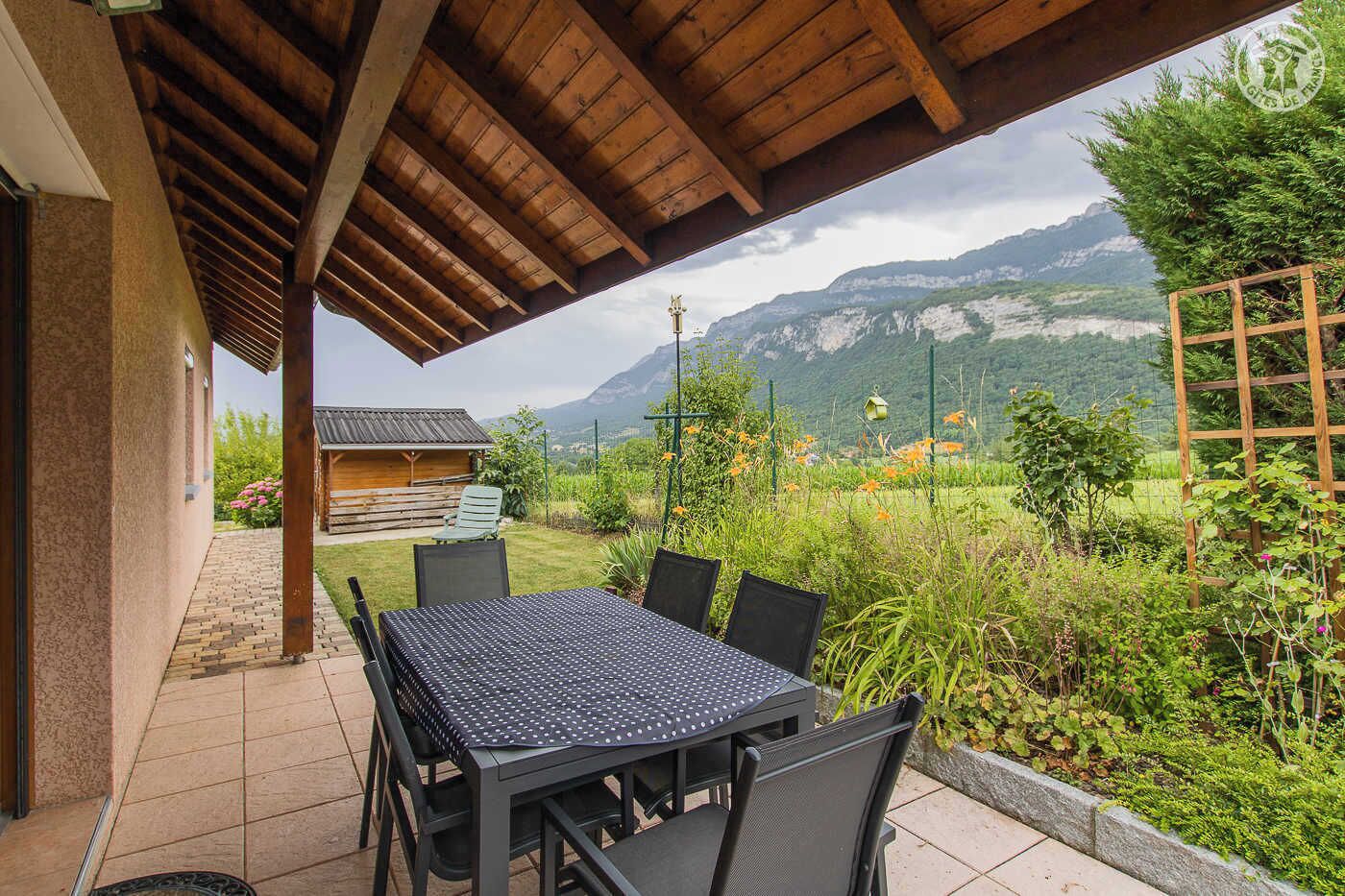 A covered patio with a table and chairs, a wooden pergola, and a view of mountains and greenery.