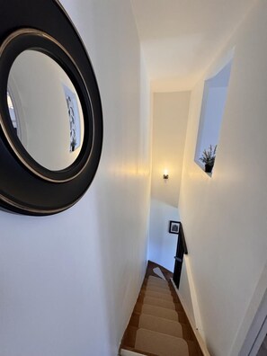A staircase with a wooden handrail, a wall-mounted mirror, and a small potted plant.