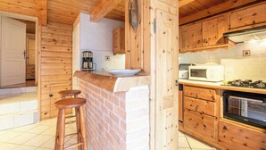 A wooden cabin interior with a kitchen area, including a stove, microwave, and bar stools.