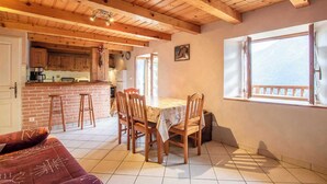 A cozy kitchen with wooden beams, a dining area with a table and chairs, and a large window with a view.