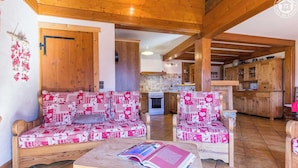 A cozy living room with a patterned sofa and armchairs, a wooden coffee table with a book, and a kitchen in the background. - CHALET LA RUIDE - HAUTELUCE LES SAISIES (HAUTELUCE LES SAISIES)