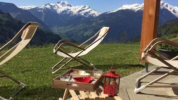 Des fauteuils de jardin avec une petite table et une lanterne, placés devant un paysage de montagnes enneigées.