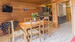 A wooden interior with a dining table, chairs, a TV, and a kitchen area.