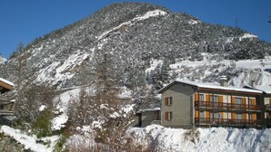 A mountain with snow-covered slopes and a building with balconies and windows.