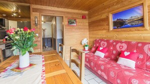 A cozy room with wooden walls, a dining table with a vase of flowers, a red sofa with heart patterns, and a framed picture on the wall.