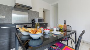 Una cocina moderna con una mesa de comedor dispuesta para el desayuno, incluyendo pan, bollería y bebidas.