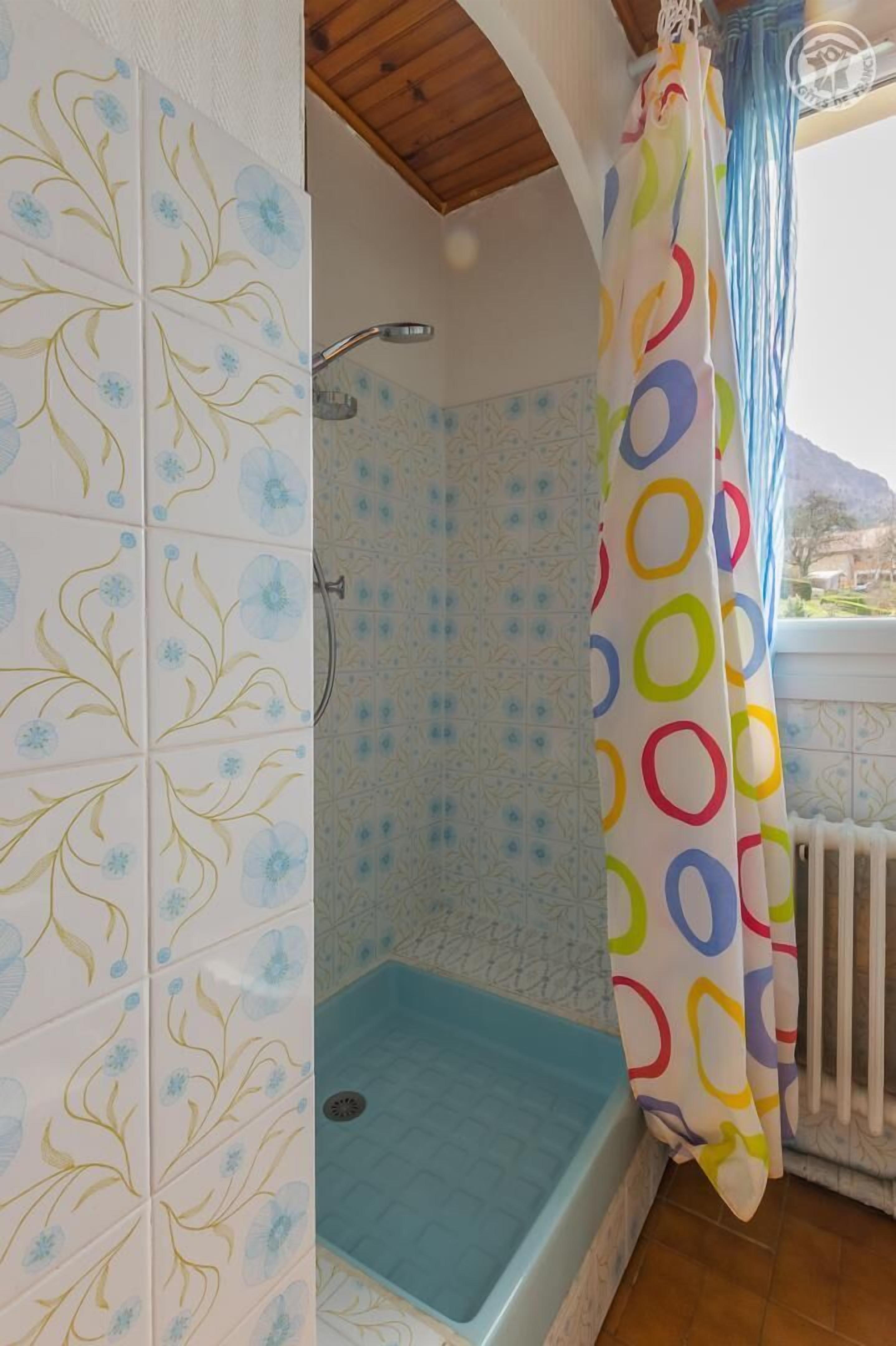 A shower area with a blue floor, a showerhead, and a colorful curtain.