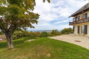 A house with a gravel driveway, a tree in the foreground, and a view of the landscape in the background.