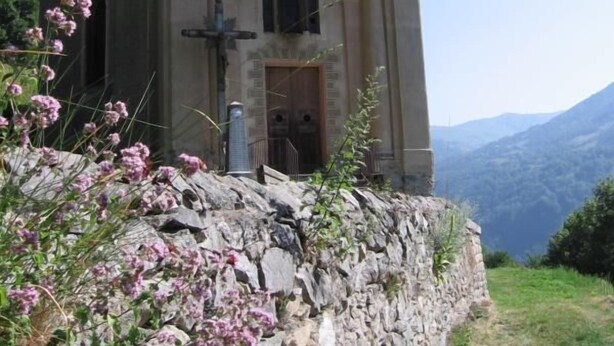 Une petite église en pierre dotée d’un clocher, située sur une colline et offrant une vue dégagée sur le paysage environnant.