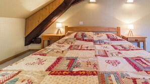 Une chambre à coucher avec une tête de lit en bois, deux tables de chevet avec des lampes et une courtepointe aux motifs variés.