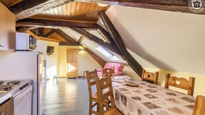 Une pièce mansardée chaleureuse, aménagée avec une table à manger, des chaises et un coin cuisine.