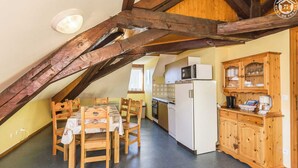 Une pièce mansardée accueillante, avec une table à manger, des chaises, un coin cuisine équipé d’un réfrigérateur et de meubles de rangement en bois.
