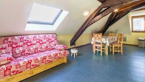 Une pièce chaleureuse avec un plafond en pente, un canapé en bois recouvert d’un tissu à motifs, une table à manger avec des chaises et une lucarne.