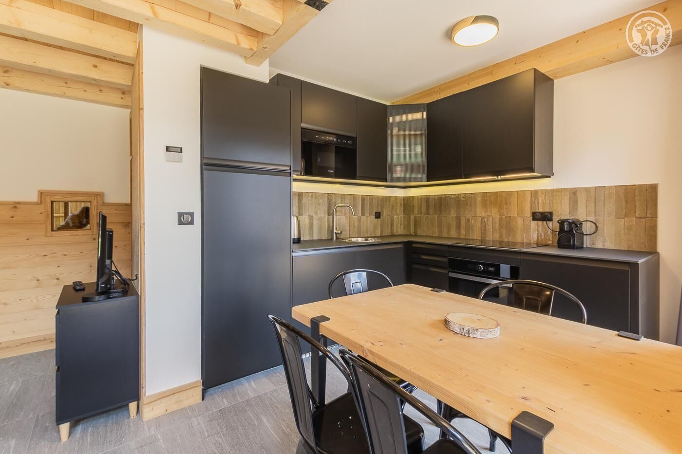 Une cuisine moderne avec des meubles de couleur sombre, une table à manger en bois et un four encastré.