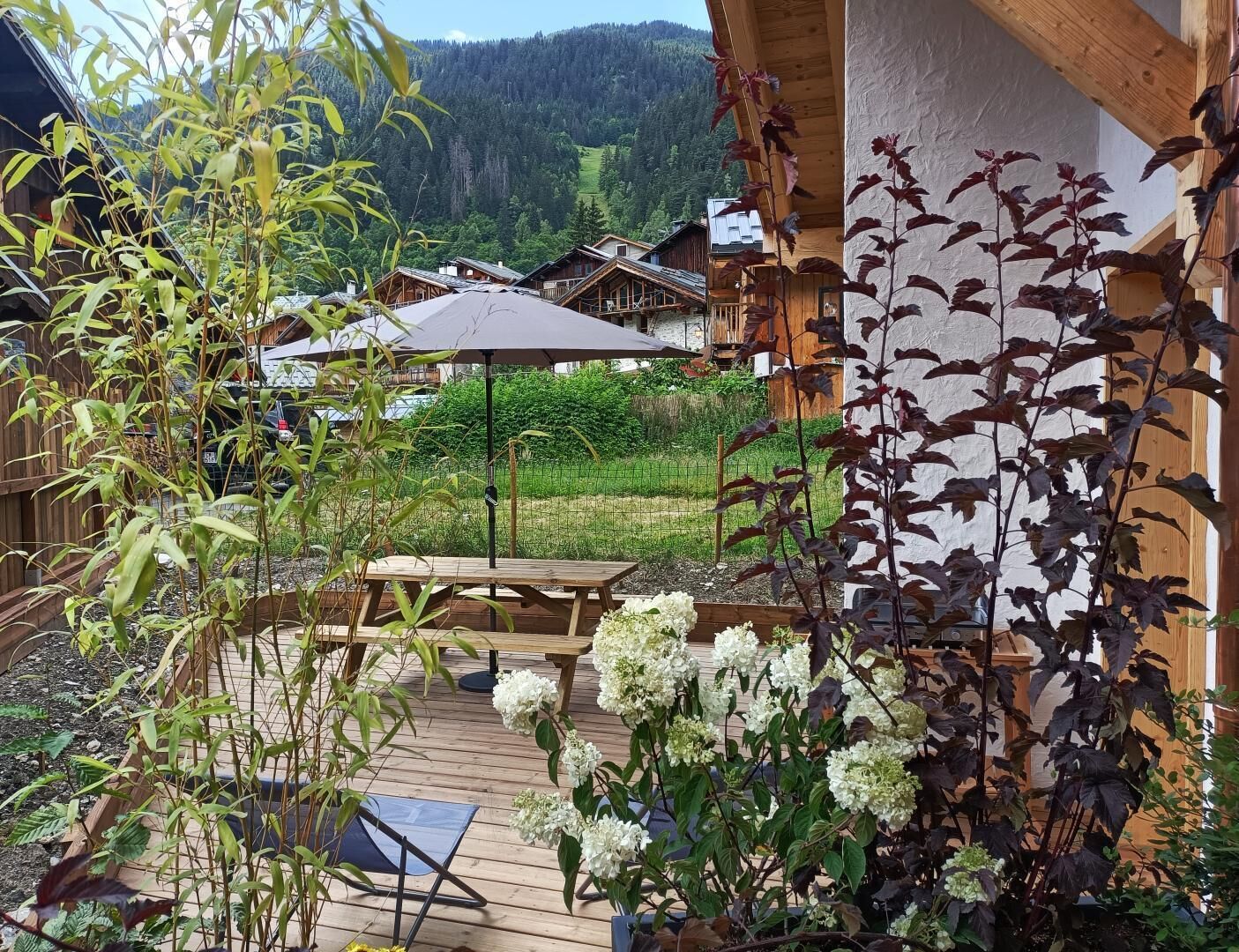 Een houten terras met een tafel en stoelen, omringd door bloempotten en bloemen.